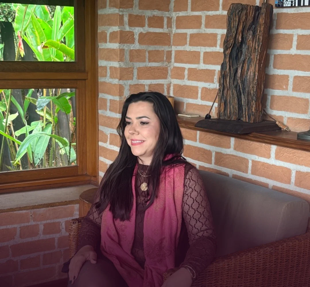 Jaque sentada num sofá junto a uma parede de tijolos, de lenço rosa, sorrindo